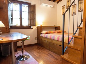 Ein Schlafzimmer mit einem hölzernen Bett, einem Schreibtisch mit Stuhl, einem Fenster mit Vorhängen und einer Treppe.