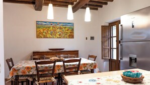A dining area with wooden chairs, a table with a floral tablecloth, a painting on the wall, and a refrigerator. - "Poggio del Pero" by Interhome (Panicale)