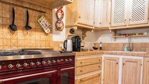 A kitchen with a red stove, wooden cabinets, a coffee maker, and a hanging pot holder. - "Poggio del Pero" by Interhome (Panicale)