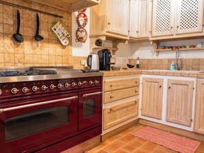A kitchen with a red stove, wooden cabinets, a coffee maker, and a hanging pot holder. - "Poggio del Pero" by Interhome (Panicale)
