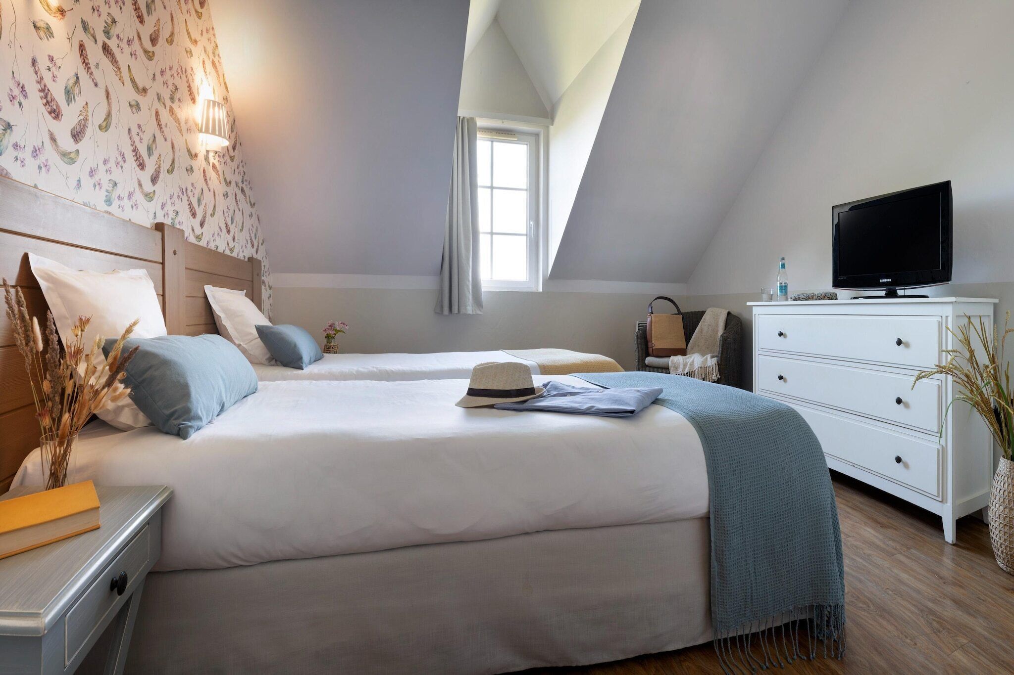 Une chambre avec deux lits, un téléviseur posé sur une commode et une fenêtre avec des rideaux.
