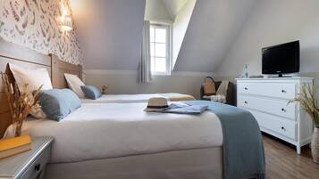 Une chambre avec deux lits, un téléviseur posé sur une commode et une fenêtre avec des rideaux.