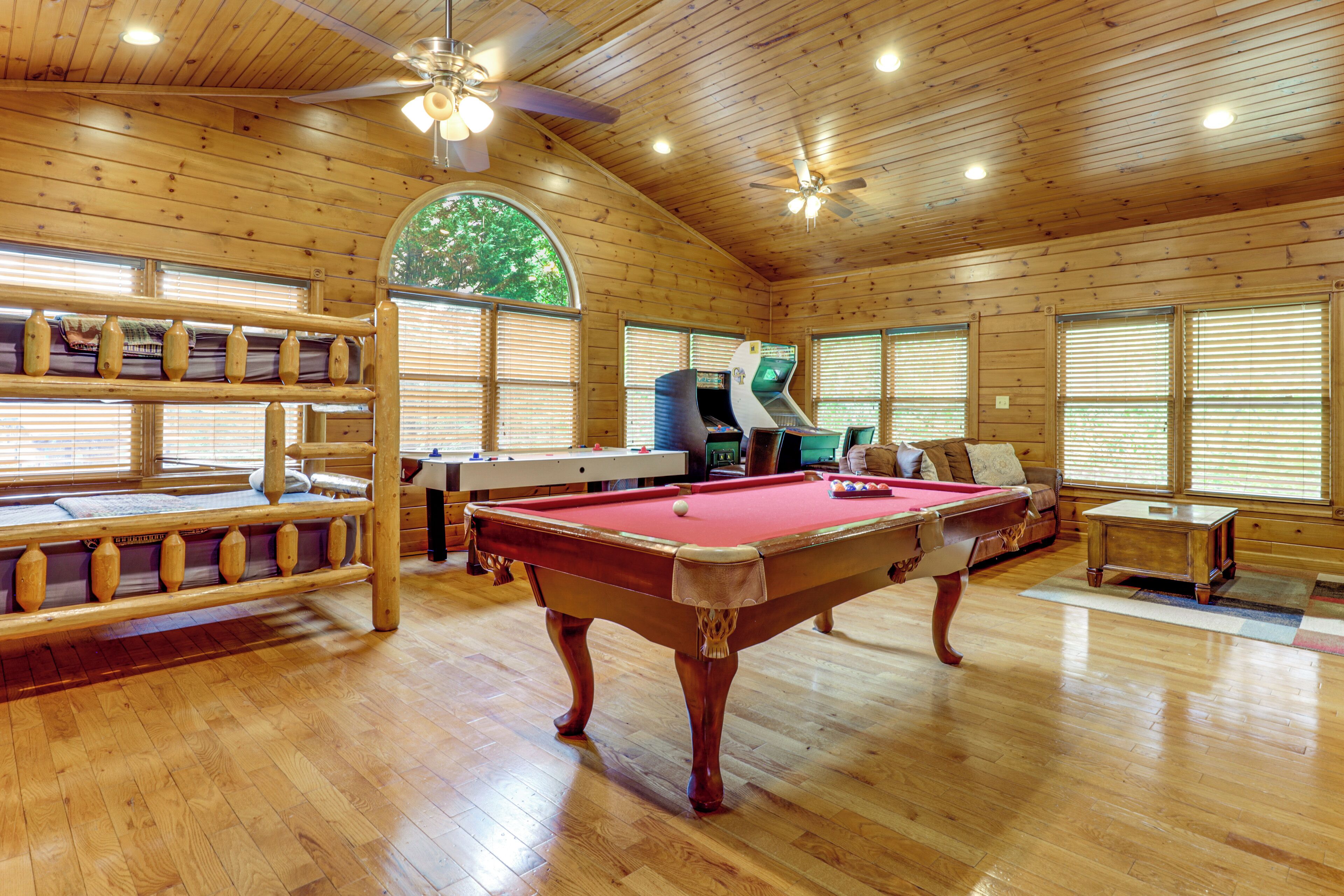 A wooden interior with a pool table, a sofa, and a ceiling fan.