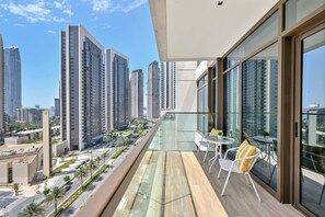 Ein Balkon mit Glasgeländer, einem Tisch und Stühlen sowie Blick auf hohe Gebäude.