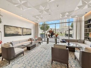 Ein modernes Wohnzimmer mit einem geometrisch gemusterten Boden, einer Sofagarnitur, einem Couchtisch und Blick auf die Stadt durch große Fenster.