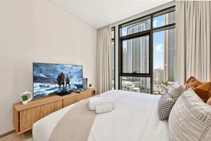 Ein Hotelzimmer mit einem großen Bett, einem Fernseher auf einer Holzkonsole, einem Fenster mit Blick auf die Stadt und einem Vorhang.
