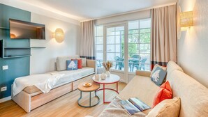 Un salon moderne avec un canapé, un petit lit, une table basse et un téléviseur fixé au mur.