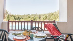 A balcony with a table set for two, overlooking a beach and forest.