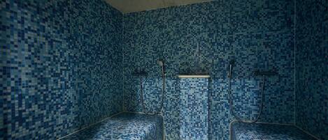 A room with mosaic blue tiles, two benches, and a shower area.