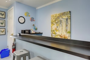 Ein Zimmer mit blauer Wand, einer Uhr, einem Gemälde, einem Regal mit einem Schild und einem Feuerlöscher.