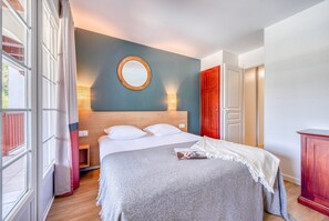 Ein Hotelzimmer mit einem Bett, einem runden Spiegel, einem Nachttisch, einem hölzernen Kopfteil, einer roten Tür und einem Holzschrank.