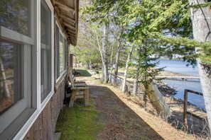 A cabin with a porch, a bench, and a view of a lake.