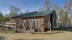 A wooden building with a green roof, a fenced area with a bench, and a dirt path leading to it. - Fun on Gull Lake! Family Cabin w/ Resort Perks (Tenstrike)
