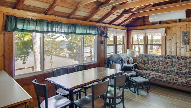 A wooden cabin interior with a dining table, chairs, a sofa, and large windows. - Fun on Gull Lake! Family Cabin w/ Resort Perks (Tenstrike)