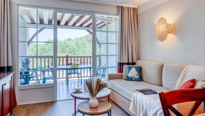 Une pièce comprenant un canapé, une petite table avec un vase, une chaise en bois et une vue sur une terrasse extérieure, accessible par une grande fenêtre.