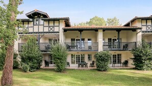 Ein zweistöckiges Gebäude mit Balkonen, einer Terrasse mit Sitzgelegenheiten im Freien und einem gepflegten Rasen.