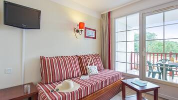 Une pièce avec un canapé à rayures, une petite table, un téléviseur fixé au mur et un balcon aménagé avec du mobilier d’extérieur.