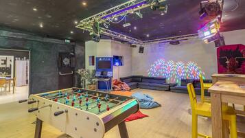 A room with a foosball table, a PS4 gaming console, a couch, and a projection screen displaying colorful patterns.