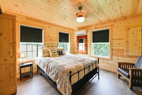 Ein Schlafzimmer in einer Holzhütte mit einem Bett, einer Bank und großen Fenstern.