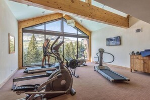 A gym with various exercise equipment, large windows, and a view of trees. - Alps Flat with Heated Pool (Flaine)