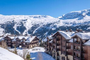 A snow-covered mountain resort with multi-story buildings, balconies, and a clear blue sky. - Alps Flat with Heated Pool (Flaine)