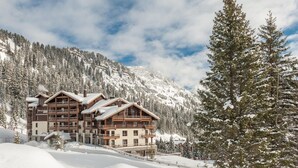 Una cabaña de varios pisos con balcones, rodeada de montañas nevadas y árboles.