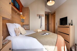 Une chambre d’hôtel comprenant un lit, une tête de lit en bois, un téléviseur, une commode en bois et un porte-serviettes fixé au mur.
