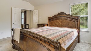 A bedroom with a wooden bed, a nightstand, a door, and a window with blinds. - Fenced Yard & Patio! Family Escape in DFW Suburbs (Fort Worth)