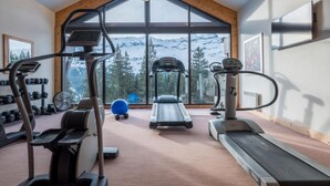 Ein Fitnessstudio mit Laufbändern, Crosstrainern und Übungsbällen, mit einem großen Fenster und Blick auf die Berge.
