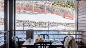 Ein Essbereich mit Tisch und Stühlen, ein Fenster mit Blick auf eine verschneite Landschaft und eine Steinwand.