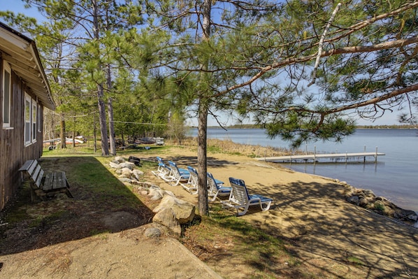 A lakeside property with a wooden cabin, a dock, and beach chairs.