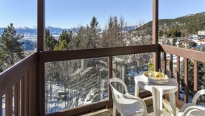 Ein Balkon mit Tisch und Stühlen mit Blick auf eine verschneite Berglandschaft.