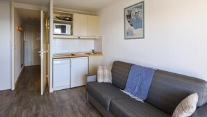 Ein kompakter Wohnbereich mit einer Küchenzeile, einem Sofa und einer Tür zu einem weiteren Raum.
