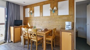 Ein Zimmer mit einer Holzwand, einem Fernseher, einem Tisch mit Stühlen, einer Kaffeemaschine und einem Schrank.