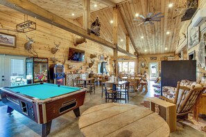 A wooden interior with a pool table, dining area, and various mounted animal heads.