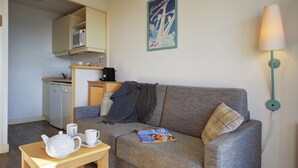 A compact living space with a kitchenette, a sofa, a table with a teapot and cups, and a wall-mounted lamp. - Stunning Pyrenees Apartment for 4 (Font Romeu Ermitage)