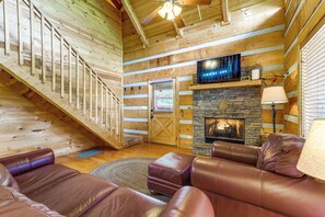 Ein Holzblockhaus-Interieur mit Kamin, Ledermöbeln, einer Treppe und einem Fernseher.