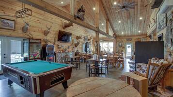 Un intérieur en bois comprenant une table de billard, un coin repas et différentes têtes d’animaux montées au mur.