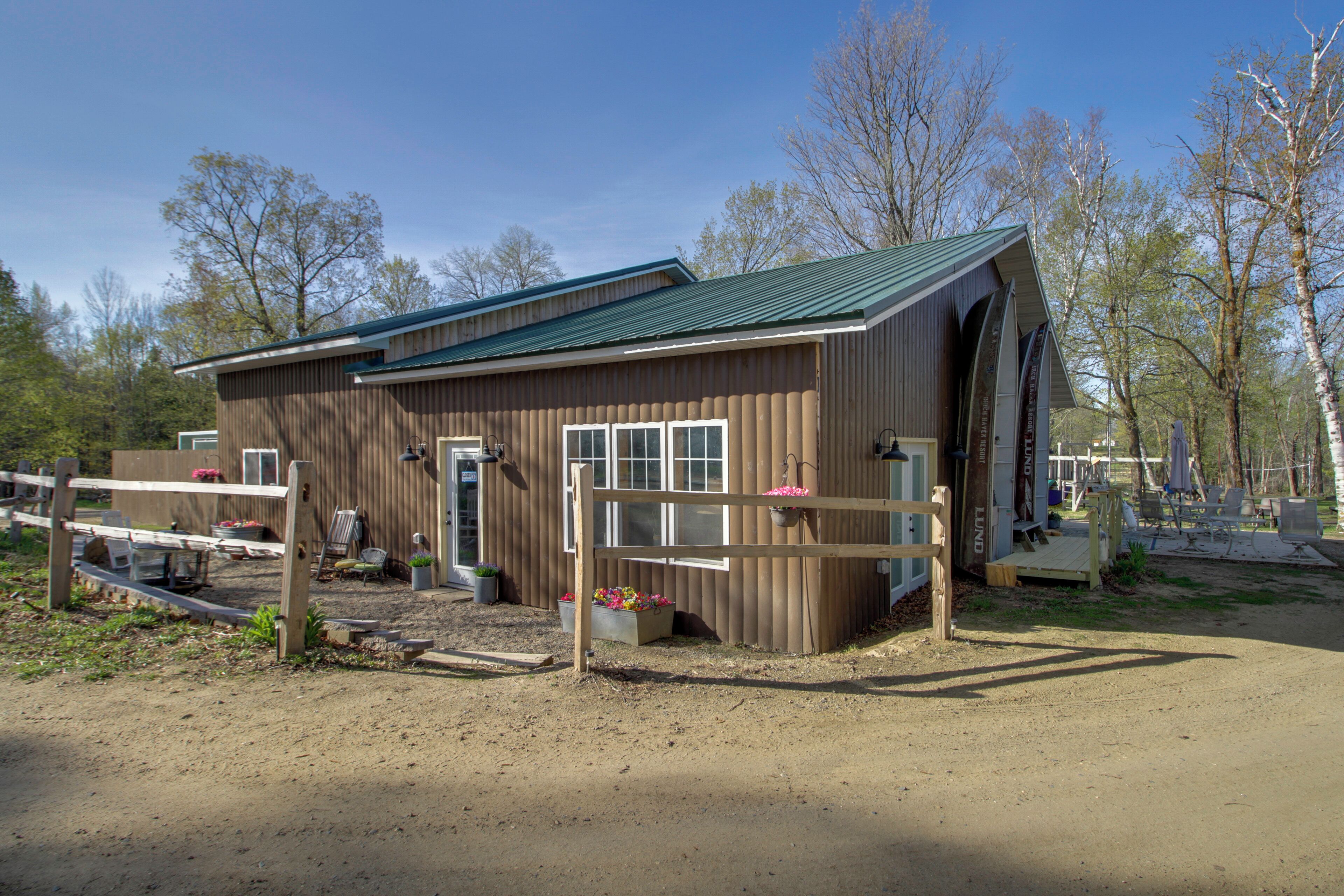 Un bâtiment en bois surmonté d’un toit végétalisé, une zone délimitée par une clôture avec un banc, et un chemin de terre qui y mène.