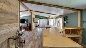 A spacious room with wooden flooring, a large wooden table, and a view of a bedroom with a bed and a TV. - Birch Haven Resort Cabin w/ Deck: Boating On-Site (Tenstrike)
