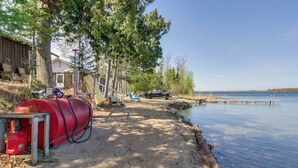 A lakeside property with a red propane tank, a wooden dock, and a vehicle parked near the water. - Birch Haven Resort Cabin w/ Deck: Boating On-Site (Tenstrike)