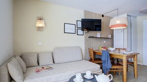 Ein modernes Wohnzimmer mit einer Couch, einem Esstisch mit Stühlen, einem an der Wand montierten Fernseher und einer Lampe.