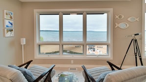 A room with a large window overlooking a beach, two chairs, a telescope, and wall art. - Rooftop Deck, Bay Views! Traverse City Penthouse (Traverse City)