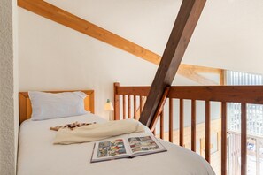 A bedroom with a wooden headboard, a bed with white bedding, a book, and a window with a view. - Luxury Duplex Apartment in Pyrenees (Font Romeu Ermitage)