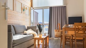 Una sala moderna con un sofá, una mesa de madera, una mesa de comedor con sillas, un televisor y vistas a montañas a través de amplios ventanales.