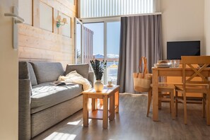 A modern living room with a sofa, a wooden table, a dining table with chairs, a TV, and a view of mountains through large windows. - Luxury Duplex Apartment in Pyrenees (Font Romeu Ermitage)