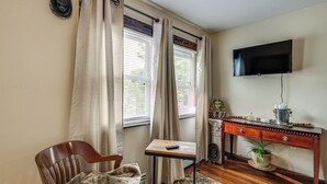 Ein Zimmer mit einem Holzbett, einem kleinen Tisch mit einer Fernbedienung, einem Schreibtisch mit einem Fernseher und einer Zimmerpflanze.