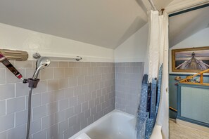Et badeværelse med badekar, brusehoved og flisebeklædt væg.
