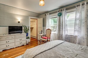 Un dormitorio con cama, cómoda, televisor, silla y ventana con cortinas.