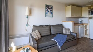 Ein Wohnzimmer mit Sofa, Lampe, Küchenzeile und einer Wand mit einem Poster.